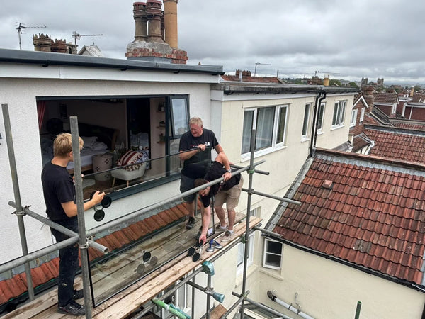 Glazing team installing large picture window from rooftop scaffolding in Redland, Bristol